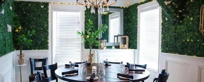 A stylish dining area featuring a round wooden table set with glassware and black napkins, surrounded by black chairs.